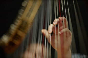 Close up on hand of female musician playing harp instrument plucking strings softly with fingers while performing enchanting melody on stage, copy space