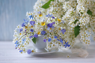 Still life with a bouquet of spring white flowers of bird cherry, blue pansies, scilla and brunnera...