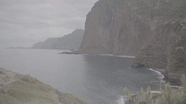 Steep coastal cliffs with lush vegetation rising from blue Atlantic Ocean on Madeira, Portugal, under an overcast sky (SLOG3)