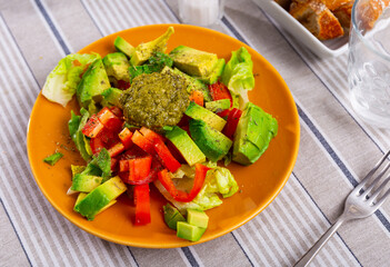 Mixed salad made from Chinese cabbage, bell pepper, avocado slices and green pesto sauce. Dish complemented with pieces of baguette, glass of wine.