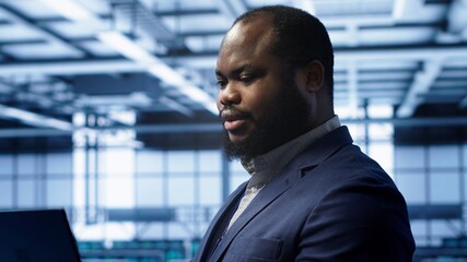 Admin in server farm using laptop to patch network issues leading to slow data transfer rates. Close up of IT specialist in data center workspace fixing errors affecting supercomputers, camera A