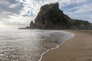 Woman enjoying the Piha  beach at low tide, waves gently lapping at the shore. Tranquil coastal scene. PIHA, AUCKLAND, NEW ZEALAND