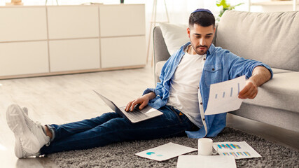 Paperwork Concept. Portrait of young jewish man working at home office, holding and reading paper...