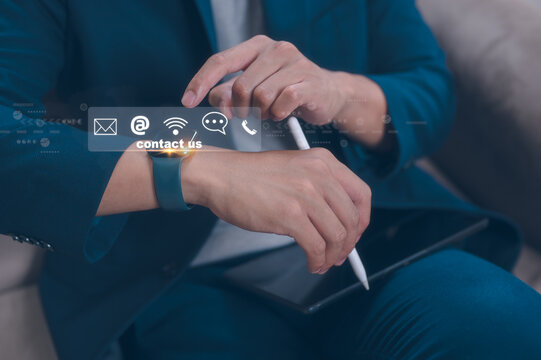Businessman sitting on sofa in office using smartwatch and virtual icons in concept of contact us hot line customer service and support - Powered by Adobe