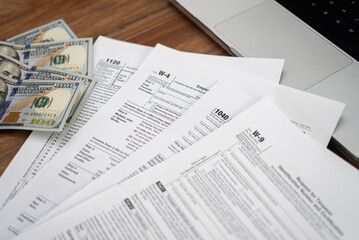 Tax forms and dollar bills on a wooden desk with a laptop. Financial management, tax refund, and accounting concept. 
