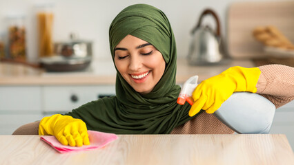 Closeup portrait of happy islamic housewife in hijab and protecitve yellow rubber gloves cleaning...