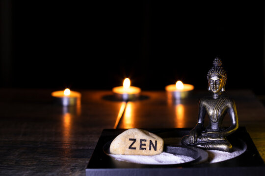 Ambiente de meditaci&oacute;n: velas encendidas, un buda sentado al lado de una piedra que tiene escrita la palabra zen, luz c&aacute;lida