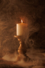 Fototapeta premium Lit candle on a wooden holder in low light. Warm candle glow.