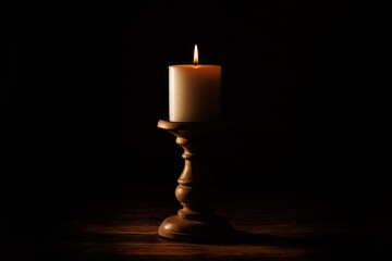 Lit candle on a wooden holder in low light. Warm candle glow.