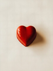 Red Heart-Shaped Chocolate: A single, perfectly shaped red heart-shaped chocolate captured from a top-down angle on a smooth white background