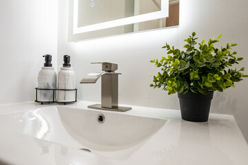 Fototapeta premium Modern bathroom sink with sleek faucet, marble soap dispensers, and a small potted plant. Clean and minimalist design.
