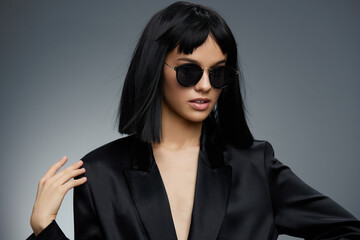 Black suit, sunglasses, woman posing on gray background, hand on hip a confident woman in a sleek black suit and sunglasses strikes a powerful pose against a gray backdrop, her hand resting