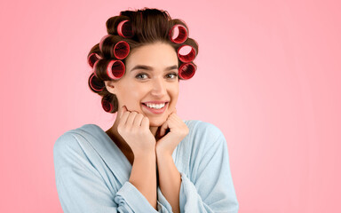 Portrait Of Happy Lady With Hair Curlers Smiling To Camera Posing Holding Hands Near Chin Standing Over Yellow Studio Background. Headshot Of Cheerful Glamorous Housewife. Female Beauty Concept