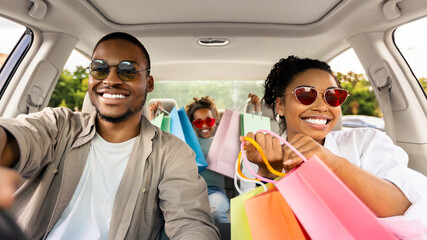 Family Shopping. Happy Black Parents And Daughter Riding Car Holding Colorful Shopper Bags After...