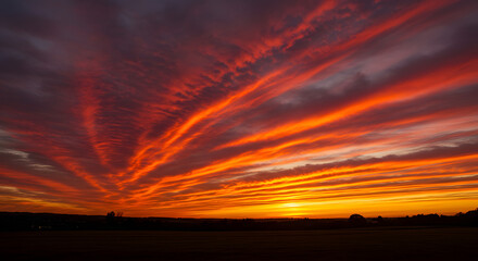 Fototapeta premium Fiery red and orange clouds create abstract streaks across the canvas of the sunset sky.