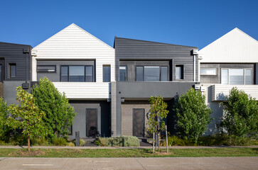 A row of modern, contemporary-style townhouses in an Australian suburb, featuring small front...