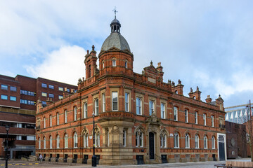 Fototapeta premium Beautiful Victorian-era building with intricate red-brick and stonework details in Manchester, UK. This architectural gem features arched windows, a central dome