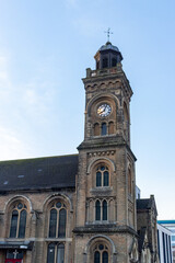 A historic church in Bournemouth, UK, featuring a tall clock tower with arched windows and intricate brickwork, set against a clear blue sky, showcasing classic Gothic architecture.
