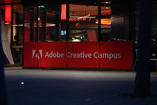 Red and white Adobe Creative Campus sign at RMIT University, in a window near an entrance, illuminated during the night
