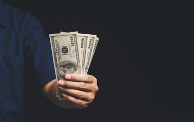 Close-up of a hand offering cash in a bundle of US dollars.