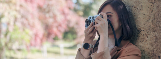 Banner Asian Women with vintage film camera take a photo. Panorama female photographer look at photo from professional camera outdoor. Young woman shooting photo in green nature park with copy space