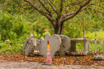 Concrete pieces and a traffic cone beneath a tree with autumn leaves on a roadside in a green...