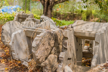 Broken concrete slabs arranged near a tree, with scattered autumn leaves and surrounding greenery, in rural South Korea
