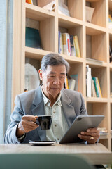 Thoughtful senior man holding coffee and using a tablet in a cozy library like cafe