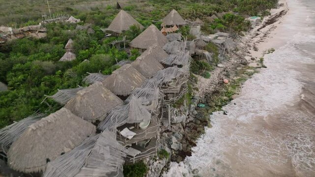 Azulik eco luxury resort wooden huts alongside Caribbean shoreline, ocean waves crashing in from Caribbean sea, Revealing drone shot