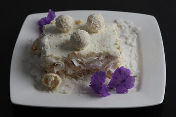 Delicious coconut cake dessert topped with chocolate balls and garnished with purple flowers on a white plate