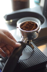 A barista holds a portafilter filled with ground coffee