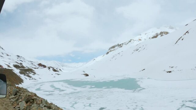 4K shot of Frozen Suraj Tal lake during winter season at Lahaul, Himachal Pradesh, India. Cold frozen lake in Himalaya mountains. Lake surrounded with snowcapped mountains. View from moving car.
