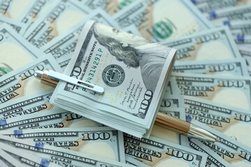 Golden pen clipping big amount of hundred dollar bills US banknotes