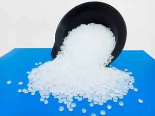 PP plastic pellets, virgin polypropylene polymer plastic granules poured from black cup into blue background, for product catalog design of plastic manufacturing industry company profile