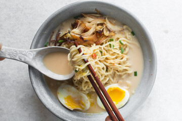 Overhead view of milk noodles in chopsticks, top view of ramen noodles in creamy chicken broth on a marble countertop