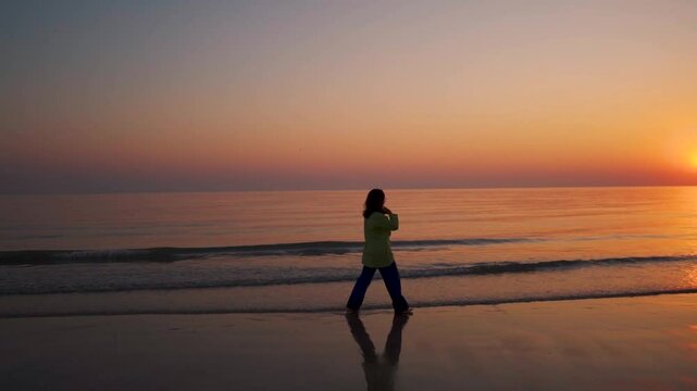 Silhouette of Young woman walking at beach during sunset at Mandvi, Gujarat, India. Sky and sea. Beautiful sunset at beach with orange sky. Reflection of woman in wet sand of beach.
