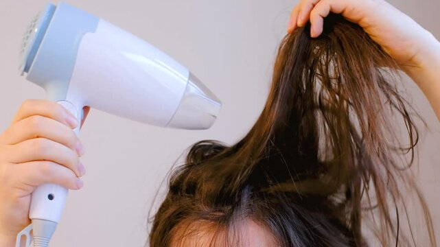Young woman drying her hair with hairdryer in the bathroom close-up front view.
