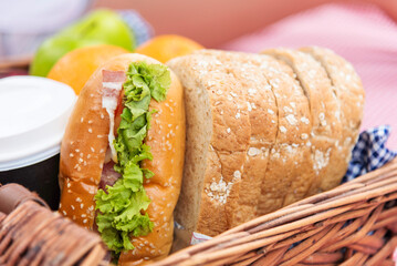 Picnic basket food bread fresh fruit coffee cup orange juice in wood wicker box on red Blanket. Wheat bakery fruit food and drinks in green park outdoor lifestyle. Breakfast healthy appetizer box.
