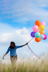 Vertical Cheerful cute girl holding balloons running on green meadow white cloud blue sky with happiness. Hands holding vibrant air balloons play on birthday party happy times sunlight outdoor