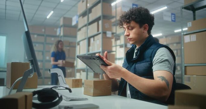 Male warehouse clerk scans parcels for delivery using tablet computer, works in postal service or online store logistics storage. Sorting center employees carrying cardboard boxes. E-commerce products