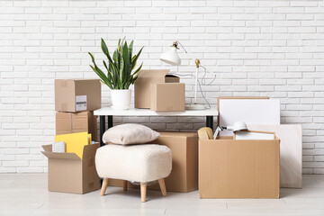 Table with houseplant and cardboard boxes near white brick wall. Moving house concept
