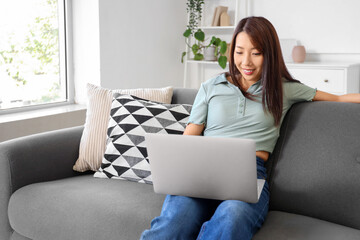 Young Asian woman with laptop sitting on sofa at home