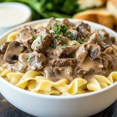 A savory and rich beef stroganoff with tender strips of beef in a creamy mushroom sauce, served over a bed of egg noodles, in a white bowl