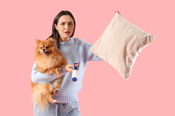 Troubled woman with pillow, lint roller and fluffy dog on pink background