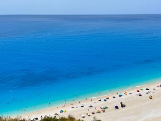 Fototapeta premium Egremni beach, Lefkada, Greece. Rich, deep blue, crystal clear water and pure white sand with colourful beach umbrellas and people swimming. 