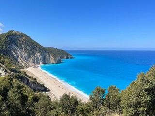 Milos beach, Lefkada, Greece landscape. Image taken from the mountain above. Featuring rich blue water, clear skies, people on the beach and shrubs in the mountain. Unreal beach and heavenly. water.  