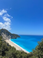 Milos beach, Lefkada, Greece landscape. Image taken from the mountain above. Featuring rich blue water, clear skies, people on the beach and shrubs in the mountain. Unreal beach and heavenly. water.  