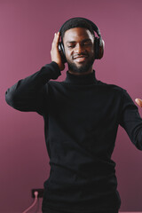 Obraz premium Young Black man enjoying music with headphones in a cozy, modern setting, wearing a black sweater, expressing joy and relaxation