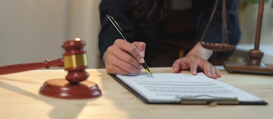 Female lawyer is signing a legal document on a clipboard, with a gavel and scales of justice on the desk, symbolizing law, justice, and legal proceedings