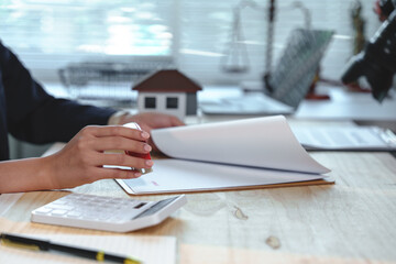 Real estate agent is stamping a document for a home purchase agreement, finalizing the sale and transfer of ownership with a small house model and scale of justice in the background